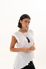 Blusa de textura rugosa en color blanco, sin mangas, con detalle de volados en los hombros y corte asimétrico en el ruedo.