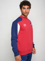 Buzo de felpa con diseño de bloques de color, predominantemente rojo en el cuerpo y azul marino en las mangas y hombros. Presenta el escudo del Club Nacional de Football y el logo de Umbro en el pecho.