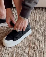 Zapatillas urbanas de lona color beige con cordones blancos y suela de goma blanca con diseño geométrico.