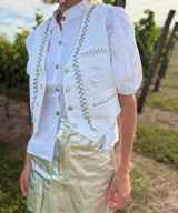 Chaleco blanco con bordados plateados a mano, con cuello mao y cierre frontal con botones. De corte recto y sin mangas.