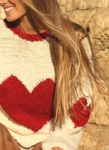 Sweater tejido de punto color marfil con cuello redondo y diseño frontal de corazón rojo. Cuenta con detalles en rojo en el borde del cuello y las mangas.