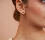 Par de caravanas doradas con forma circular y tres pequeñas piedras negras incrustadas.