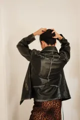 Chaqueta tipo biker de cuero sintético negro, con cuello solapa ancho, cierre asimétrico y detalles de cierres metálicos plateados.