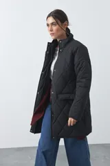 Campera capitoneada de largo medio, color negro, con cuello alto, cierre frontal con cremallera y broches a presión, y bolsillos laterales con solapa.