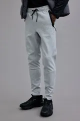 Pantalón de jogging deportivo color gris claro, de corte ajustado (slim fit), confeccionado en tejido funcional DryMove™ que absorbe el sudor. Presenta cintura elástica con cordón de ajuste negro y bolsillos laterales con cierre sellado negro.