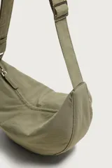Bolso de hombro de nylon color negro, con diseño curvo y cierre de cremallera en el compartimento principal. Cuenta con asa ajustable para llevar al hombro y bolsillo interior con cierre.