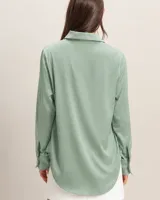 Camisa de satén color verde pistacho, con cuello clásico, cierre frontal de botones y mangas largas con puños abotonados.