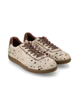 Sneaker de estilo deportivo confeccionado en cuero con pelo, con estampado de manchas tipo vaca en tonos neutros. Presenta cordones de algodón al tono y suela de goma color miel.