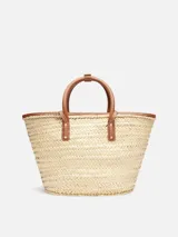 Bolso tipo canasto tejido a mano en fibra vegetal con detalles de cuero marrón, asas cortas enrolladas y logotipo Jacquemus en letras doradas en el frente.