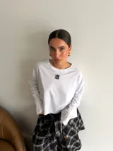 Remera de manga larga en color blanco, con corte holgado y cuello redondo. Presenta un pequeño parche rectangular con diseño gráfico en el centro del pecho.