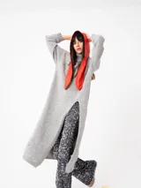 Buzo largo gris de tejido de punto grueso con cuello alto y capucha con orejas de conejo rojas. Tiene mangas largas y un tajo lateral.