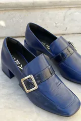 Mocasín de cuero vacuno color bordó con acabado charolado, punta cuadrada, taco bloque bajo y detalle de tira con hebilla metálica plateada en el empeine.
