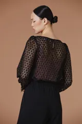 Blusa de encaje blanco con mangas largas abullonadas y puños con detalle de terminación desflecada. Presenta un diseño de cuello redondo y corte recto.