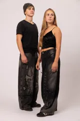 Pantalón de jean negro con proceso de lavado localizado y corte balloon fit. Presenta un diseño de recortes asimétricos, detalles de tachas metálicas y terminaciones desflecadas en el frente. Cuenta con bolsillos traseros clásicos y un calce holgado.