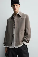 Sobrecamisa de corte relajado confeccionada en tejido compacto con lana. Presenta cuello solapa, cierre frontal con botones, mangas largas con puños abotonados y dos bolsillos de plastrón en la parte frontal.