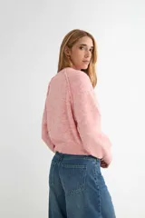 Buzo de tejido de punto con cuello redondo, diseño cropped y mangas largas con puños acanalados. Presenta una textura jaspeada en tono beige.