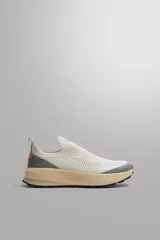 Zapatilla deportiva sin cordones de diseño técnico, con parte superior de tejido de punto transpirable en color beige. Presenta refuerzos de material protector en puntera y talón, entresuela de espuma con tecnología de rebote y suela de goma. Incluye tirador posterior para facilitar el calce.