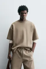 Sudadera de manga corta color marrón oscuro, con cuello redondo y bajo acabado en rib. Presenta un corte relajado y holgado (boxy fit).