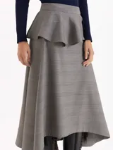 Pollera midi de corte irregular con estampado Príncipe de Gales. Presenta un diseño de falda plato con un volado caracol superpuesto en la cintura y ruedo asimétrico.