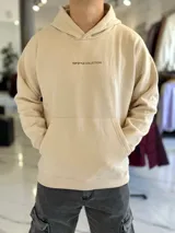 Canguro oversize de color beige con capucha y bolsillo tipo canguro al frente. En la espalda cuenta con un gran estampado tipográfico en marrón con la frase "Own Your Story", texto descriptivo y un logotipo ovalado con las letras "EST 2021".