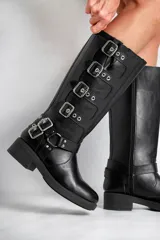 Borcegos negros de caña alta confeccionados en cuero sintético, con hebillas plateadas en los costados y cierre lateral. La altura de la caña es de 33,5 cm y la base mide 5 cm.