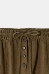 Pantalón tipo baggy de tiro bajo, confeccionado en mezcla de lino. Presenta cintura elástica con cordón ajustable, cierre frontal con botones y falsos bolsillos de vivo en los laterales.