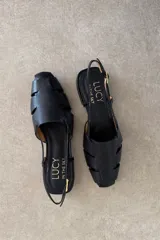 Sandalias de cuero color negro, estilo romanas con tiras entrelazadas en la parte delantera, talón descubierto y tira ajustable con hebilla metálica.