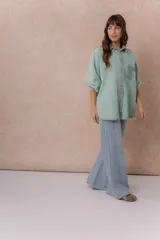 Camisa de denim color verde menta con calce relajado, cuello clásico, cierre frontal con broches metálicos, mangas largas y bolsillo aplicado en el pecho, con detalles en tono gris azulado a contraste en cuello, cartera, bolsillo y puños.