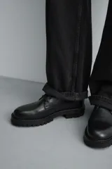 Bota tipo derby de cuero negro con cordones al tono, horma redonda y suela track con ligero tacón.