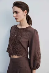 Blusa negra con detalles de apliques bordados en el pecho y las mangas, cuello redondo y mangas largas abullonadas.
