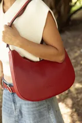 Cartera hobo de cuero color rojo con silueta curva de media luna, cierre superior y correa de hombro ajustable.