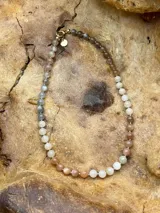 Collar corto de cuentas de piedra luna facetadas en tonos grises, blancos y durazno, con cierre de mosquetón dorado.