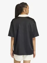 Camiseta de estilo futbolístico con cuello polo, manga corta y corte holgado. Presenta un diseño en color negro con detalles en blanco y amarillo en las mangas, y el logo de la marca junto a un estampado gráfico frontal.