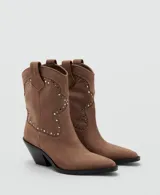 Botines de estilo texano en color marrón claro, confeccionados en piel bovina, con diseño de caña baja, puntera fina y detalles de tachas metálicas en la parte frontal y lateral.
