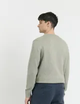 Sweater de punto en color verde claro, con cuello redondo y mangas largas. Presenta un diseño clásico de tejido liso con puños y ruedo acanalados.