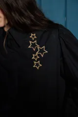 Camisa de corte clásico color blanco, con mangas largas abullonadas en los hombros y puños abotonados. Presenta un detalle de estrellas bordadas en color dorado sobre el lado izquierdo del pecho.