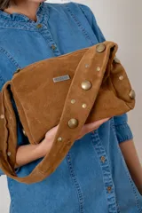 Cartera de hombro con diseño de animal print tipo vaca en tonos marrón y blanco. Presenta una correa ancha de gamuza marrón y una placa metálica con logo en el frente.