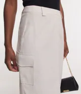 Falda midi color crema, de corte recto, con bolsillos laterales y cierre frontal.