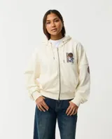 Canguro color marfil con capucha y cierre frontal, con gran estampado multicolor en la espalda que incluye las leyendas 'Born in Australia' y 'Surfing the World'.
