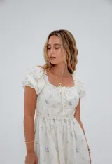 Vestido midi blanco con estampado floral celeste, escote cuadrado con detalle de lazo, mangas cortas abullonadas y falda con volados.