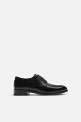 Zapato de vestir de cuero negro, tipo derby, con horma en punta y suela con ligero tacón.