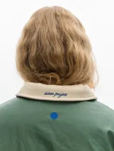 Campera verde con cuello de piel sintética blanca, cierre de botones a presión, bolsillos frontales y elástico en el dobladillo inferior. El forro interior es de algodón estampado.