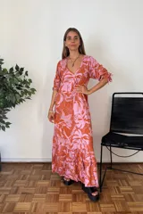 Vestido largo con estampado de hojas tropicales en tonos naranja y rosado. Presenta escote en V, mangas cortas abullonadas con ajuste de lazo y falda con volados en el ruedo.