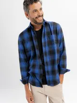 Camisa de franela a cuadros en tonos azul y negro, con cuello clásico, cierre frontal de botones y bolsillo en el pecho.