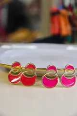 Par de caravanas con forma geométrica circular, con borde dorado y relleno de esmalte color fucsia y rojo.