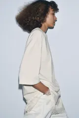 Remera color crema de algodón, corte recto, cuello redondo y mangas cortas. Presenta un panel asimétrico de encaje en el ruedo.