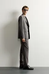 Blazer gris de corte regular fit con patrón a cuadros, confeccionada en tejido con mezcla de lana. Cuenta con cuello de solapa de muesca, cierre frontal de botonadura sencilla, bolsillos con solapa en la cadera, bolsillo de vivo en el pecho y aberturas en la espalda.