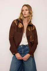 Sobrecamisa de gamuza color marrón con apliques de cuero metalizado en tono cobre en los hombros y bolsillo frontal. Presenta detalles bordados en las mangas, el bolsillo y la espalda, con un diseño de corte recto y cuello camisero.