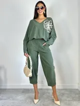 Sweater de punto oversized color verde, con escote en V y manga larga. Presenta un aplique bordado en forma de flor en el hombro izquierdo.