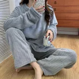 Conjunto de pijama de dos piezas confeccionado en tela de plush texturizada con diseño de rayas verticales en relieve. Incluye una remera de manga larga con cuello redondo y un pantalón de corte holgado. La remera presenta un pequeño bordado decorativo en el pecho.